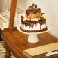Wedding cake with white frosting and fudge drizzle on Love is Sweet White Ceramic Cake Stand with scalloped edge and gilded details shown with boxed cake serving set - Special Occasion Serveware for Wedding, Anniversary, or Bridal Shower | oak7west.com