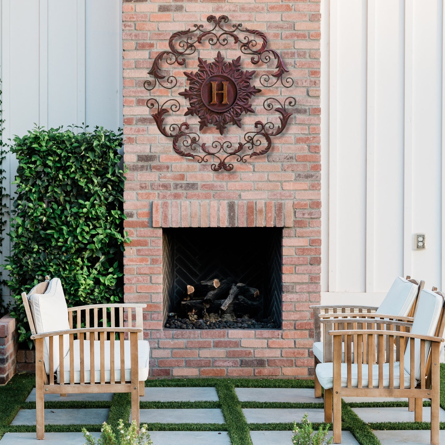 Outdoor patio with brick fireplace, wooden chairs, and decorative wall art | Monogrammed Iron Wall Grille - Personalized Wall Decor (33"W) | oak7west.com