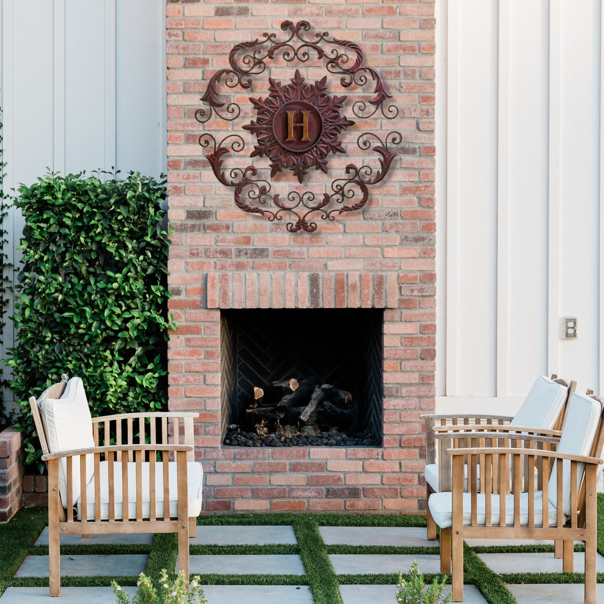 Outdoor patio with brick fireplace, wooden chairs, and decorative wall art | Monogrammed Iron Wall Grille - Personalized Wall Decor (33"W) | oak7west.com
