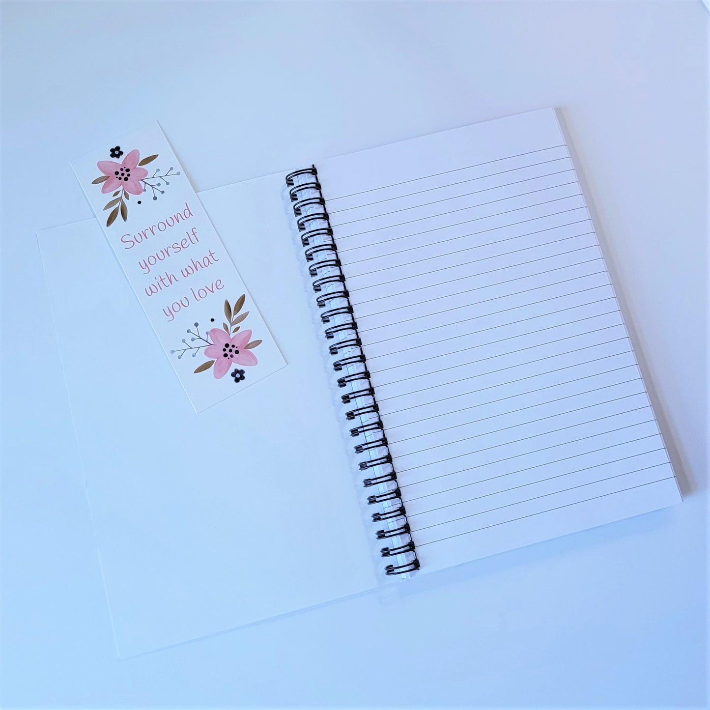 Our exclusive notebook designed in-house has a cute floral print in pinks, tans, and navy blue. The cover reads "Surround yourself with what you love" in a fun pink font. The floral design also decorates the back cover with the words "be a blessing... today, tomorrow, always". Picture shows inside lined paper with matching bookmark FREE with purchase of notebook. | oak7west.com