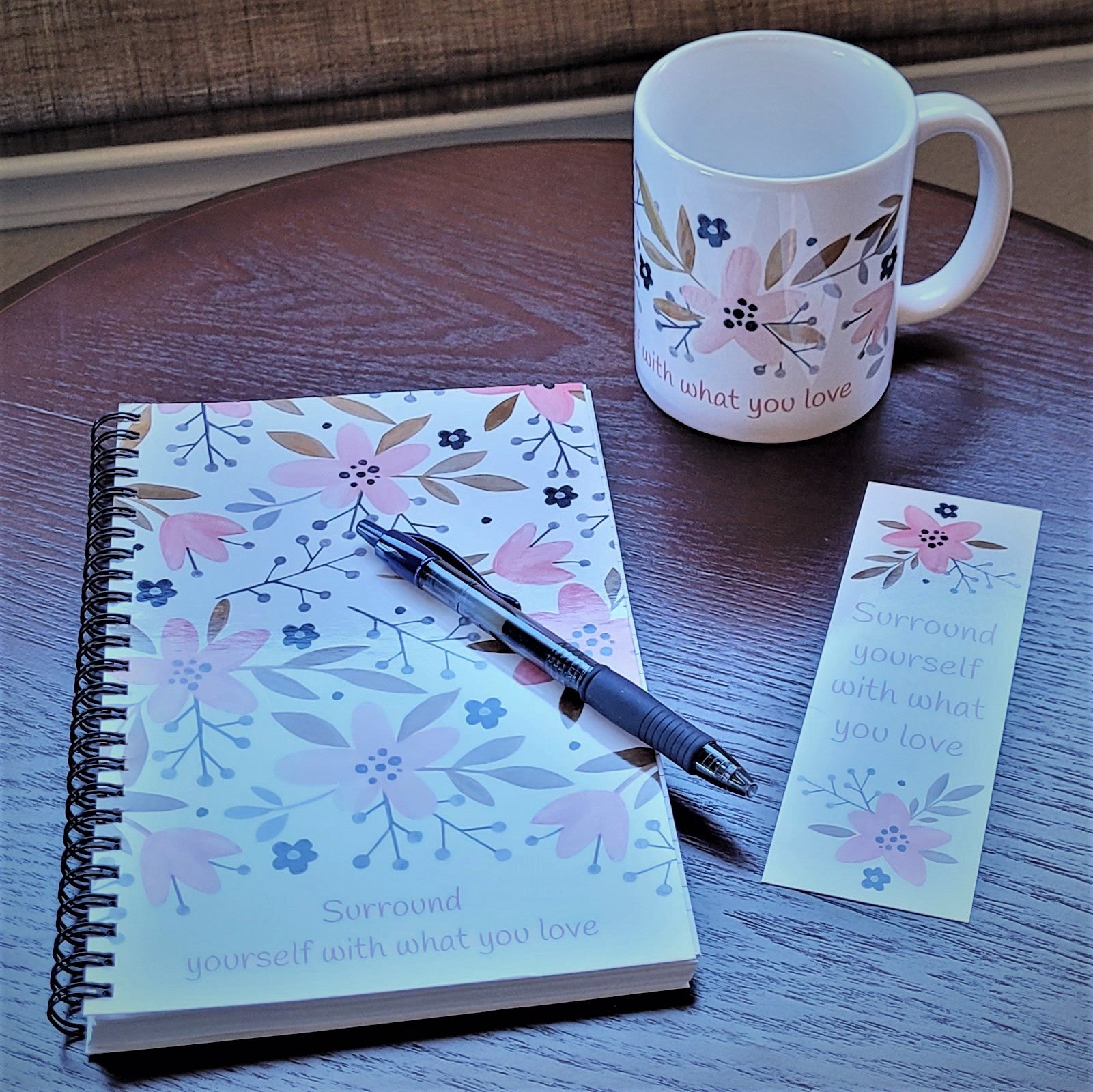 Our exclusive notebook designed in-house has a cute floral print in pinks, tans, and navy blue. The cover reads "Surround yourself with what you love" in a fun pink font. The floral design also decorates the back cover with the words "be a blessing... today, tomorrow, always". | Shown with matching bookmark and pen both FREE with purchase of notebook. | Also pictured with matching Surround yourself with what you love coffee cup - sold separately | oak7west.com