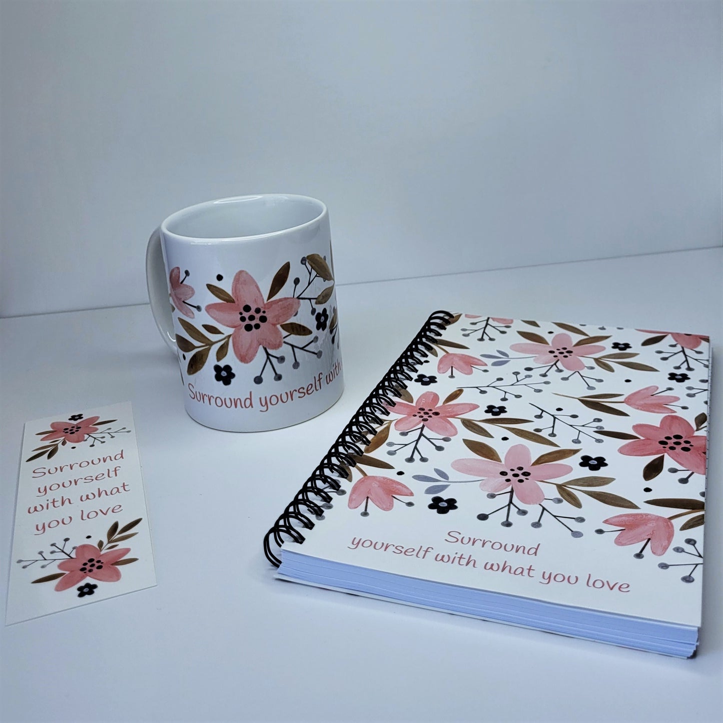 Our exclusive notebook designed in-house has a cute floral print in pinks, tans, and navy blue. The cover reads "Surround yourself with what you love" in a fun pink font. The floral design also decorates the back cover with the words "be a blessing... today, tomorrow, always". | Shown with matching bookmark FREE with purchase of notebook. | Also pictured with matching Surround yourself with what you love coffee cup - sold separately | oak7west.com