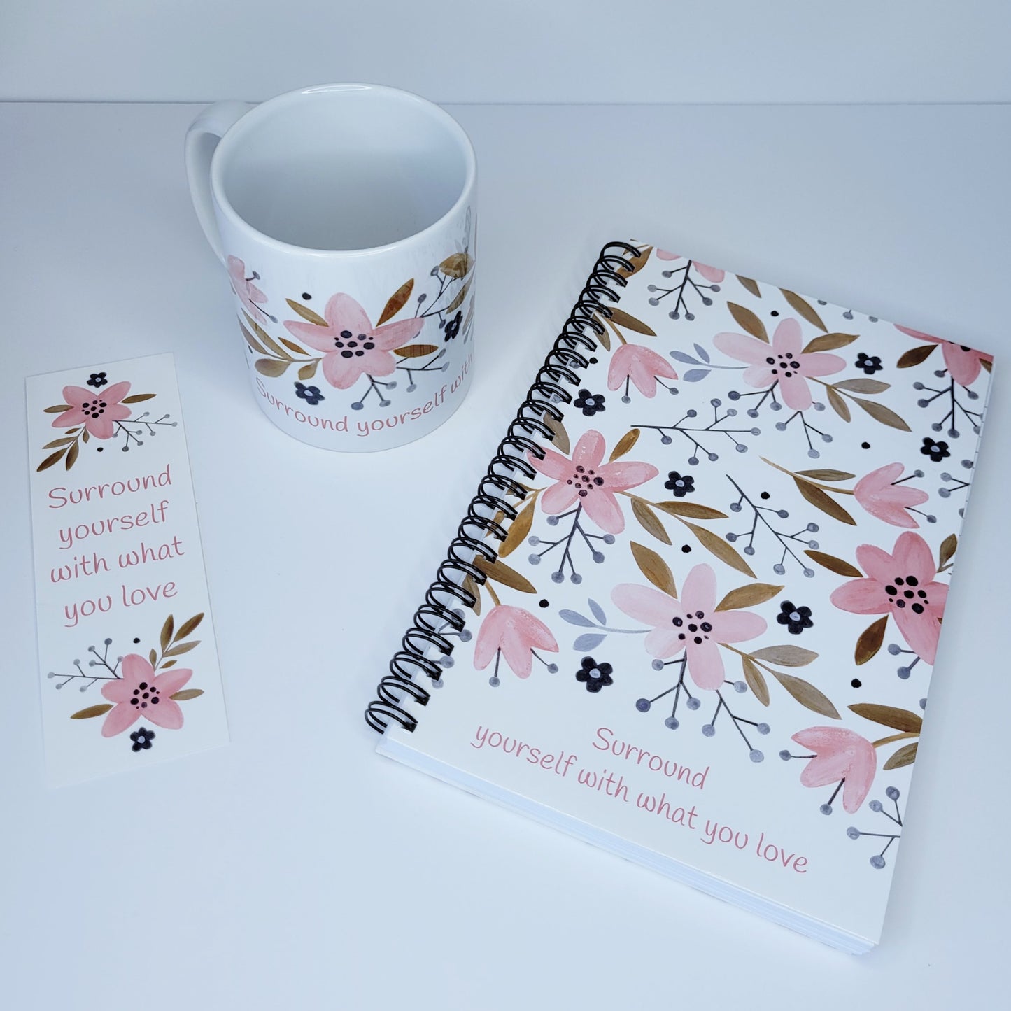 Surround yourself with what you love coffee mug (exclusive design) | lovely crisp white with a floral print in pinks, tans, and navy blue, finished off with the words "Surround yourself with what you love" in a fun pink font | 11 ounce coffee cup | shown with matching Surround yourself with what you love spiral notebook and bookmark | oak7west.com